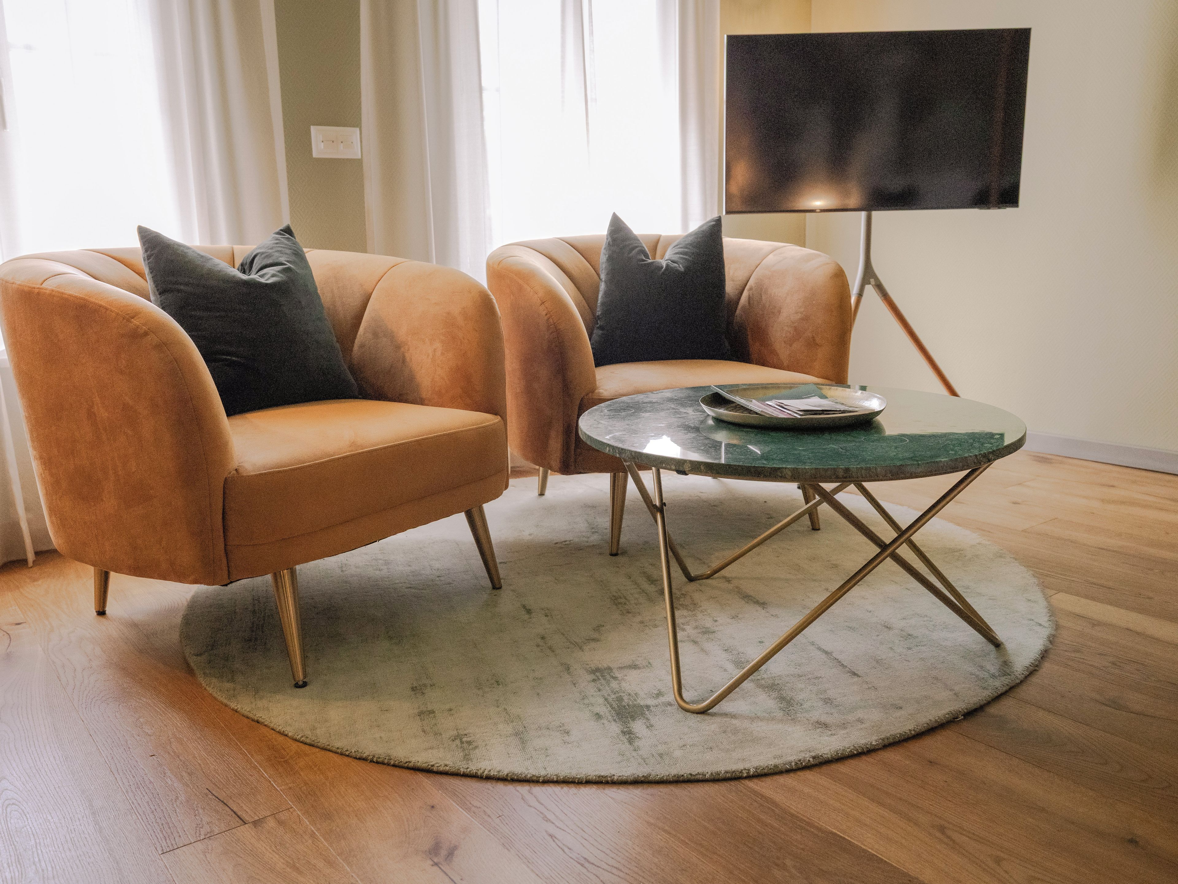 A room with two armchairs, a round table, and a flat-screen TV on a stand.