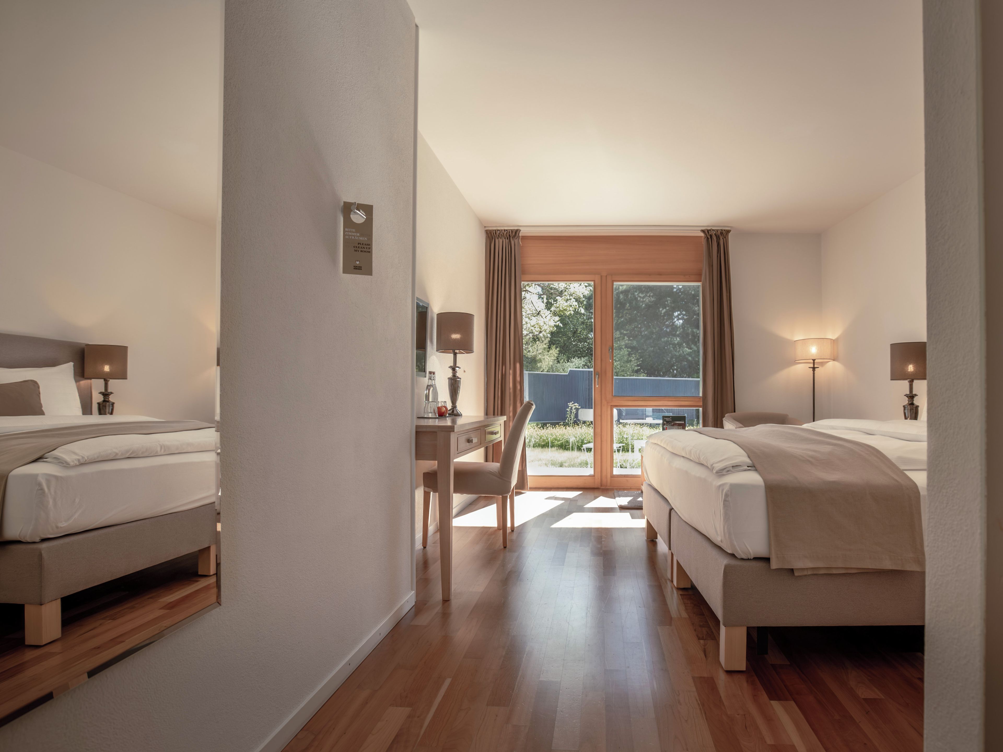 A hotel room with two beds, a desk, and a view of the outdoors.