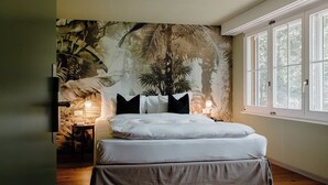 A bedroom with a bed, a nightstand, a lamp, and a window with a view of trees. - Schloss Huenigen (Konolfingen)