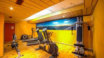 A gym with various exercise equipment, wooden floors, and a mural on the wall.