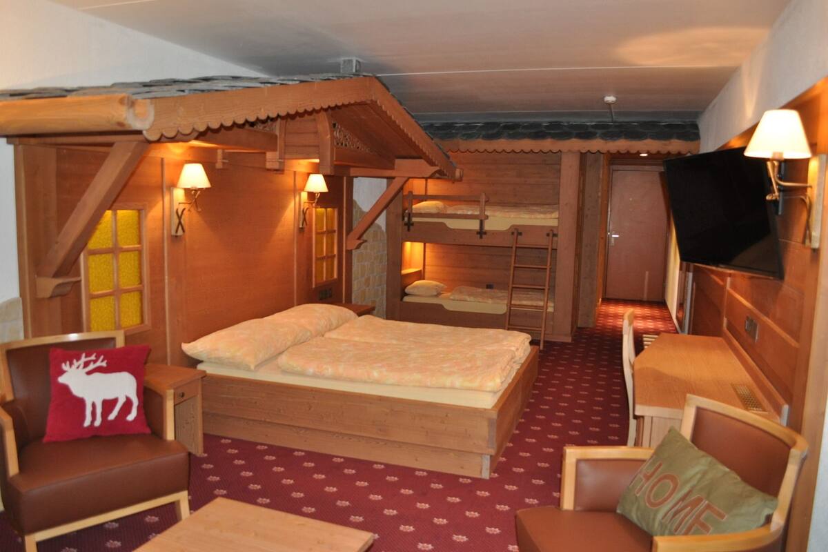 Une pièce chaleureuse en bois, avec un lit, deux chaises, une petite table et un téléviseur.