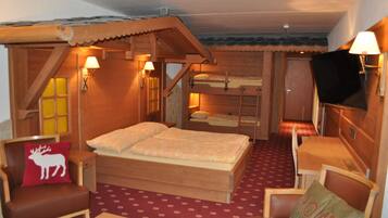 A cozy wooden room with a bed, two chairs, a small table, and a TV.