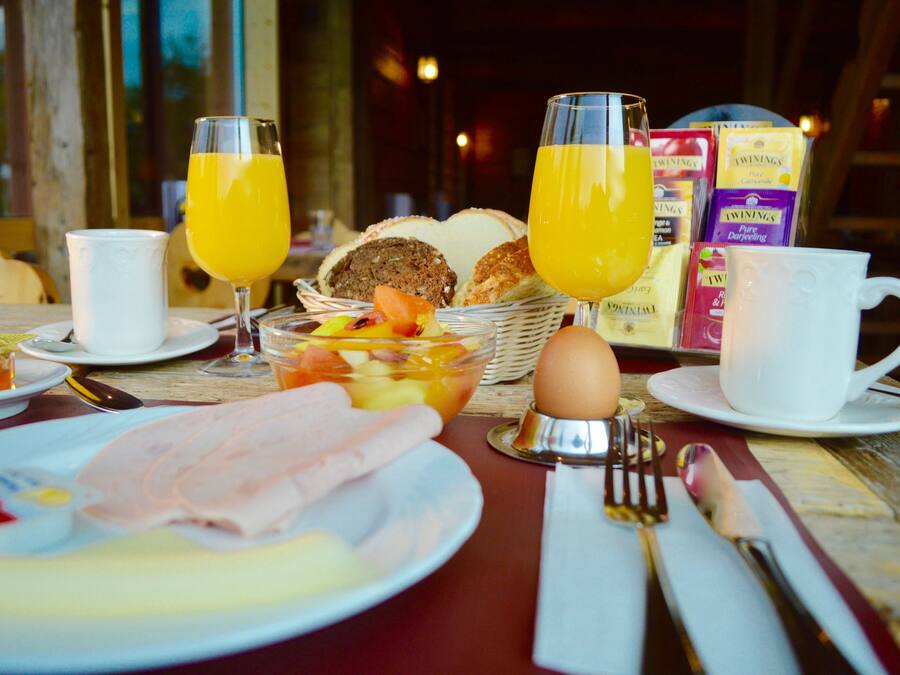 A breakfast setting with a table set for two, including plates with food, glasses of orange juice, and a basket of bread.