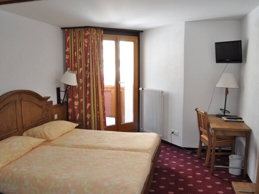 Habitación de hotel con dos camas, un escritorio con una silla, un televisor y una ventana con cortinas.