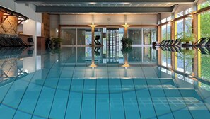 A large indoor swimming pool with clear glass walls, a central entrance, and potted plants. - Hôtel Central Résidence (Leysin)