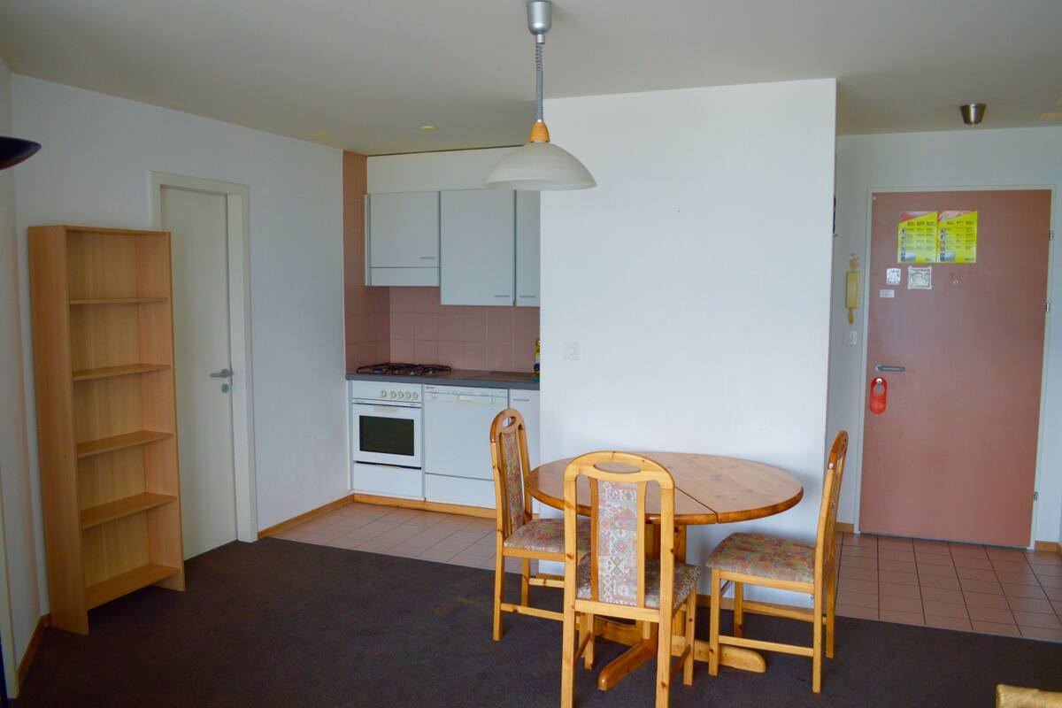 Une cuisine compacte avec des meubles blancs, une cuisinière et un coin repas comprenant une table et des chaises en bois.