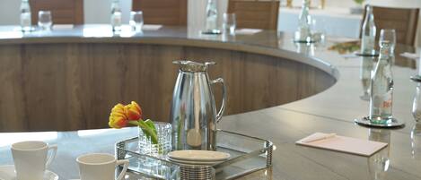 A modern dining area with a curved glass table, white plates, cups, and a pitcher.