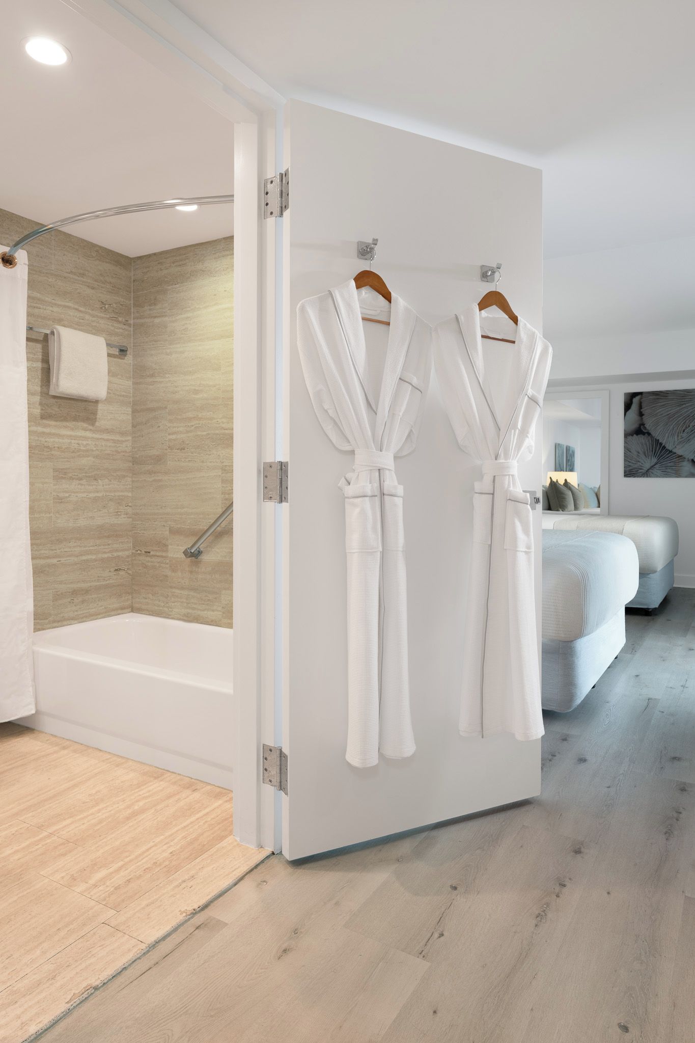 A modern bathroom with a shower, a bathtub, and two white robes hanging on hooks.