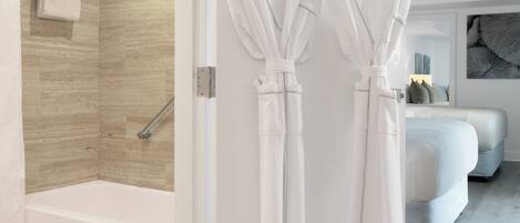 A modern bathroom with a shower, a bathtub, and two white robes hanging on hooks.