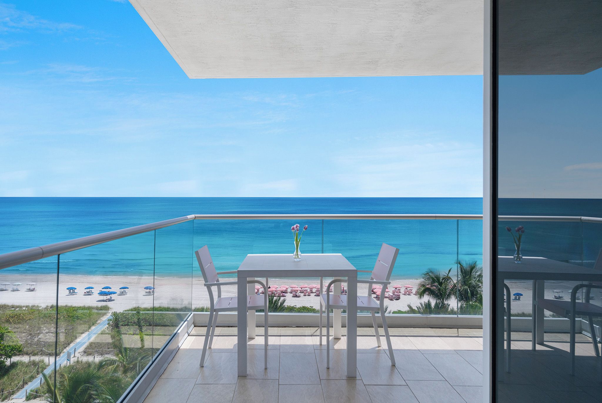 A balcony with a table and chairs overlooking a beach with umbrellas.