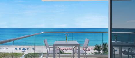 A balcony with a table and chairs overlooking a beach with umbrellas.