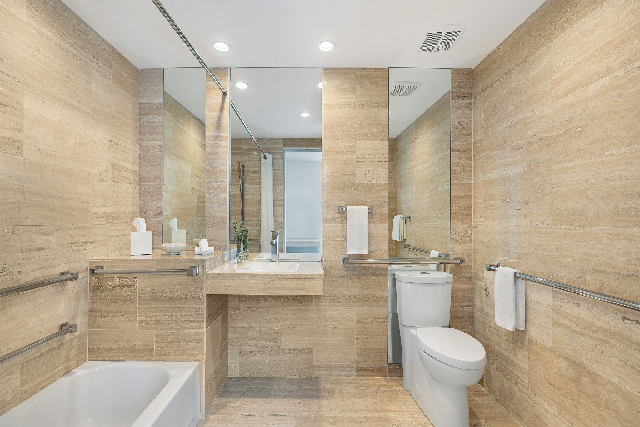 Une salle de bain moderne équipée d’une baignoire, de toilettes et d’un lavabo, avec un miroir, des porte-serviettes et une cabine de douche en verre.