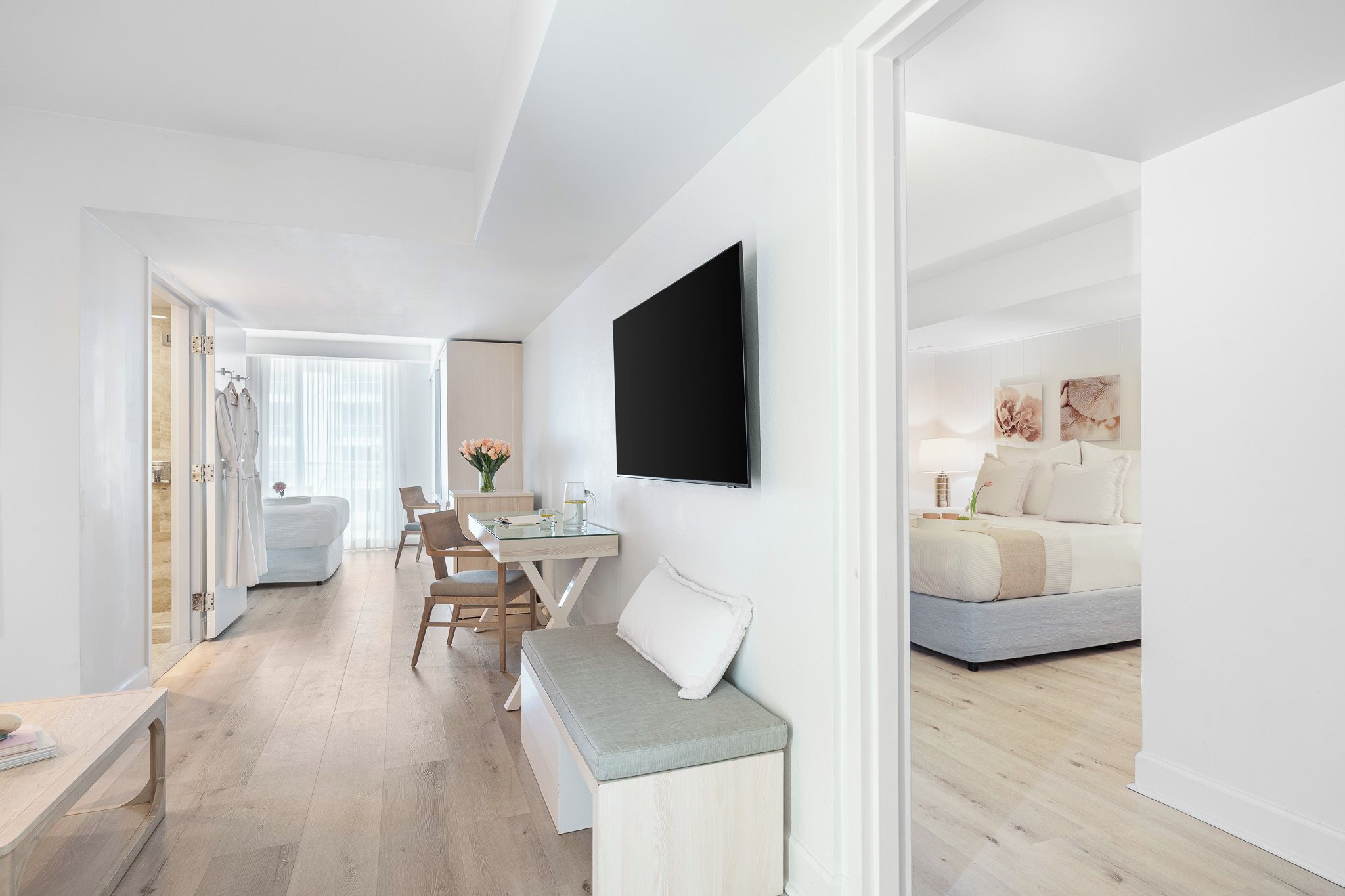 A modern hotel room with a flat-screen TV, a sofa, a dining area with a table and chairs, and a shower area.