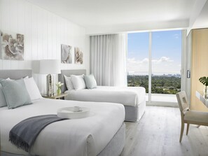 A modern hotel room with two beds, a large window with a city view, and a balcony.