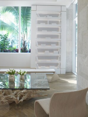 A modern interior with a glass coffee table, a white partition, and a view of tropical plants.
