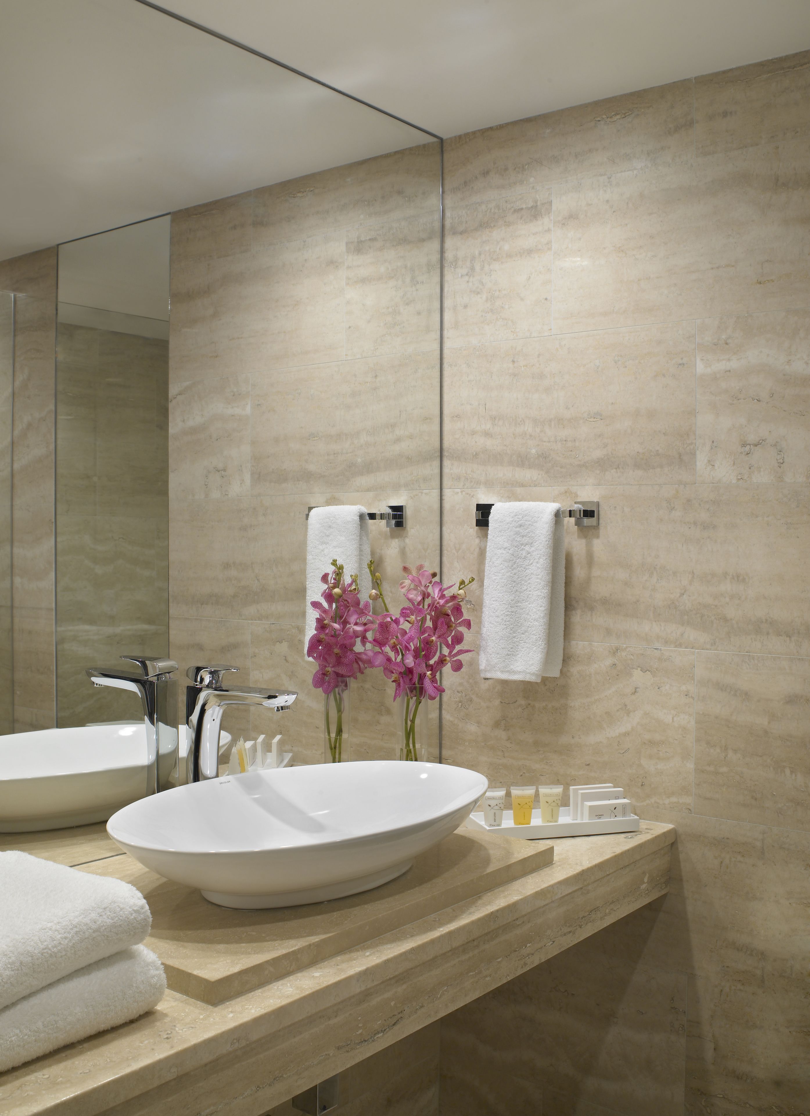 A modern bathroom with two sinks, a large mirror, and a vase with pink orchids.