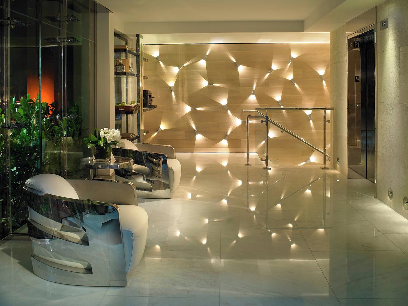 A modern lobby with a reflective floor, a seating area with a vase of flowers, and a geometric wall design.