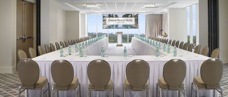 A conference room with a long table, chairs, and a screen displaying the hotel name.