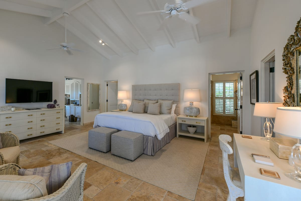 A spacious bedroom with a large bed, a television, a ceiling fan, and a bathroom visible through an open door.