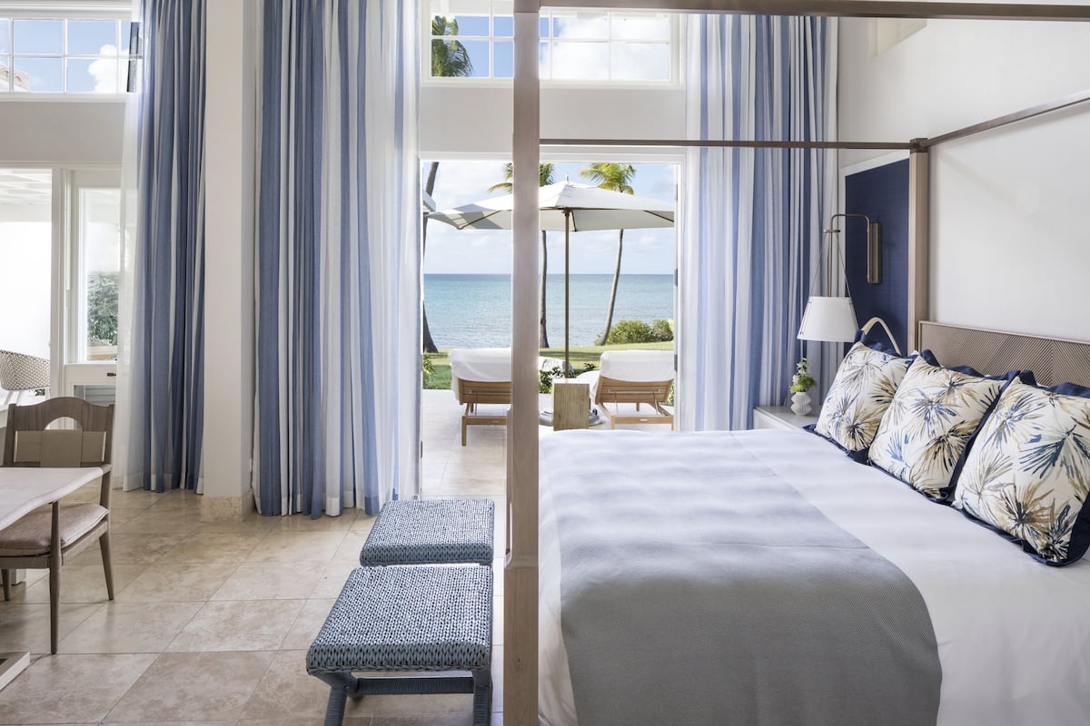 A hotel room with a large bed, a dining area, and a view of the ocean.