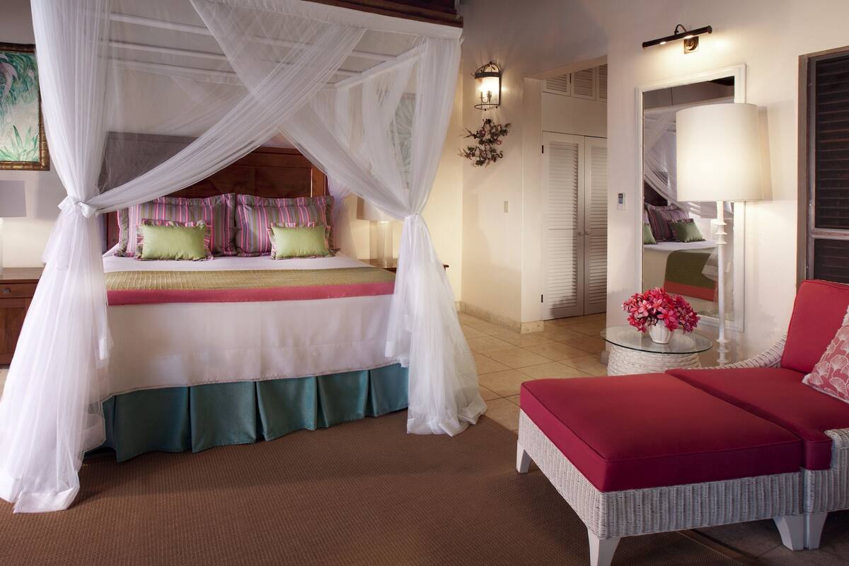 A bedroom with a four-poster bed, a red sofa, and a glass table with a vase of flowers.