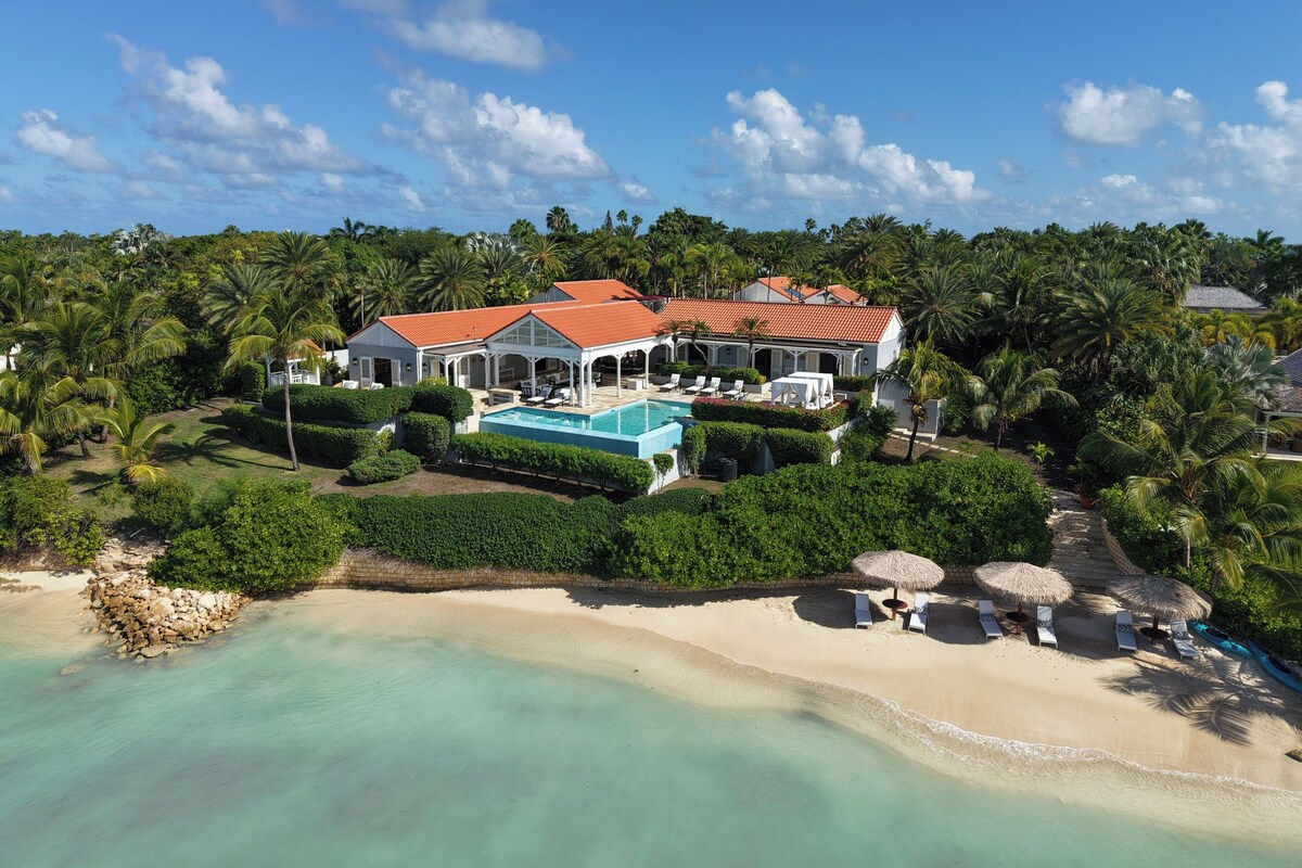 Ein Strandgrundstück mit Swimmingpool, mehreren Sitzbereichen und einem großen Haus mit rotem Dach.