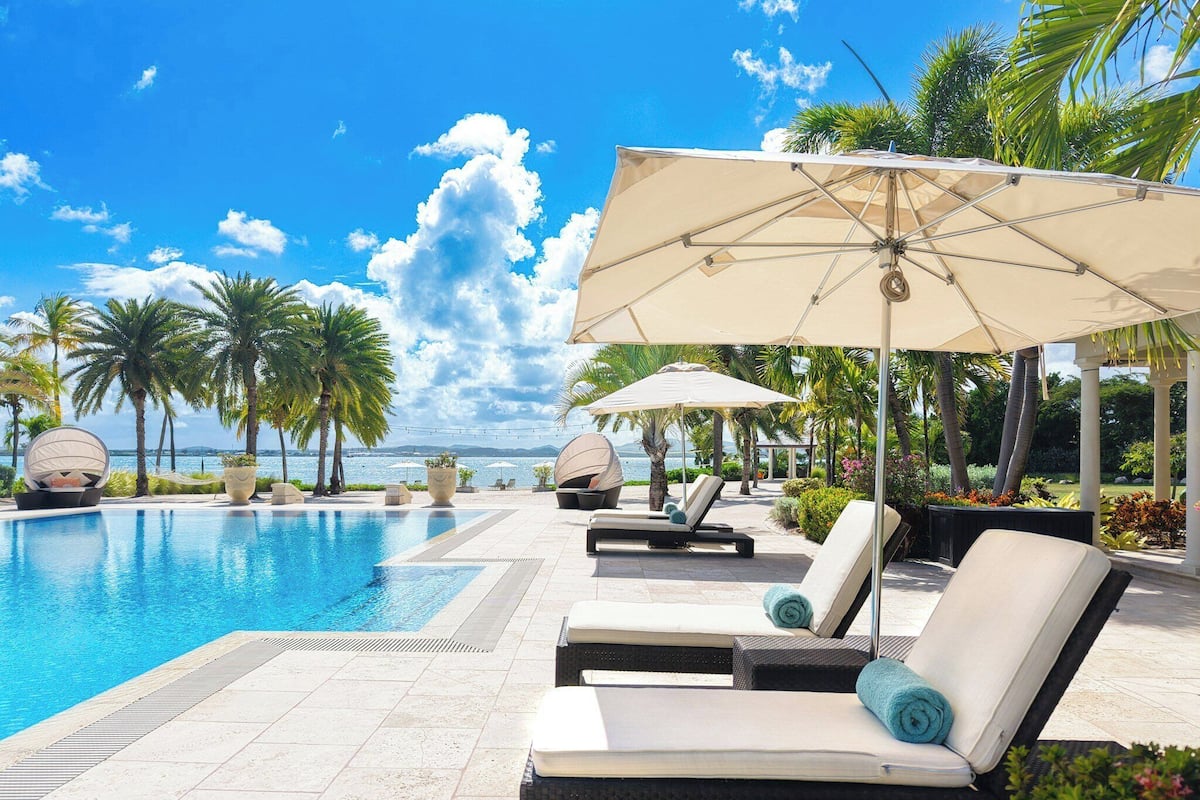 A poolside area with lounge chairs, umbrellas, and palm trees.