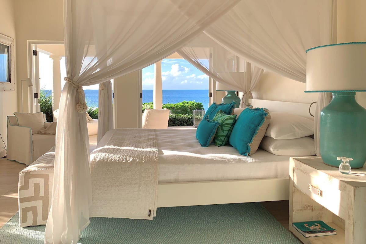 A bedroom with a bed, a nightstand, a chair, and a view of the sea.