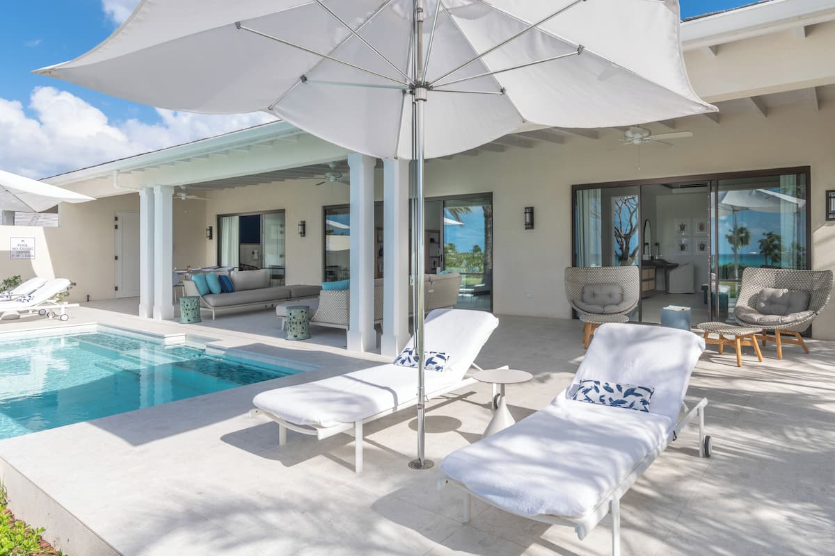 A poolside area with sun loungers, a large umbrella, and a view of the ocean.