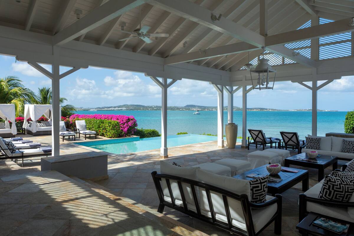 A covered outdoor area with a pool, lounge chairs, and a view of the sea.