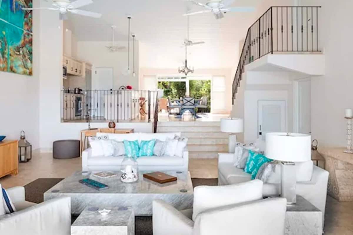 A spacious living area with a white sofa set, a marble coffee table, and a staircase leading to an upper level.
