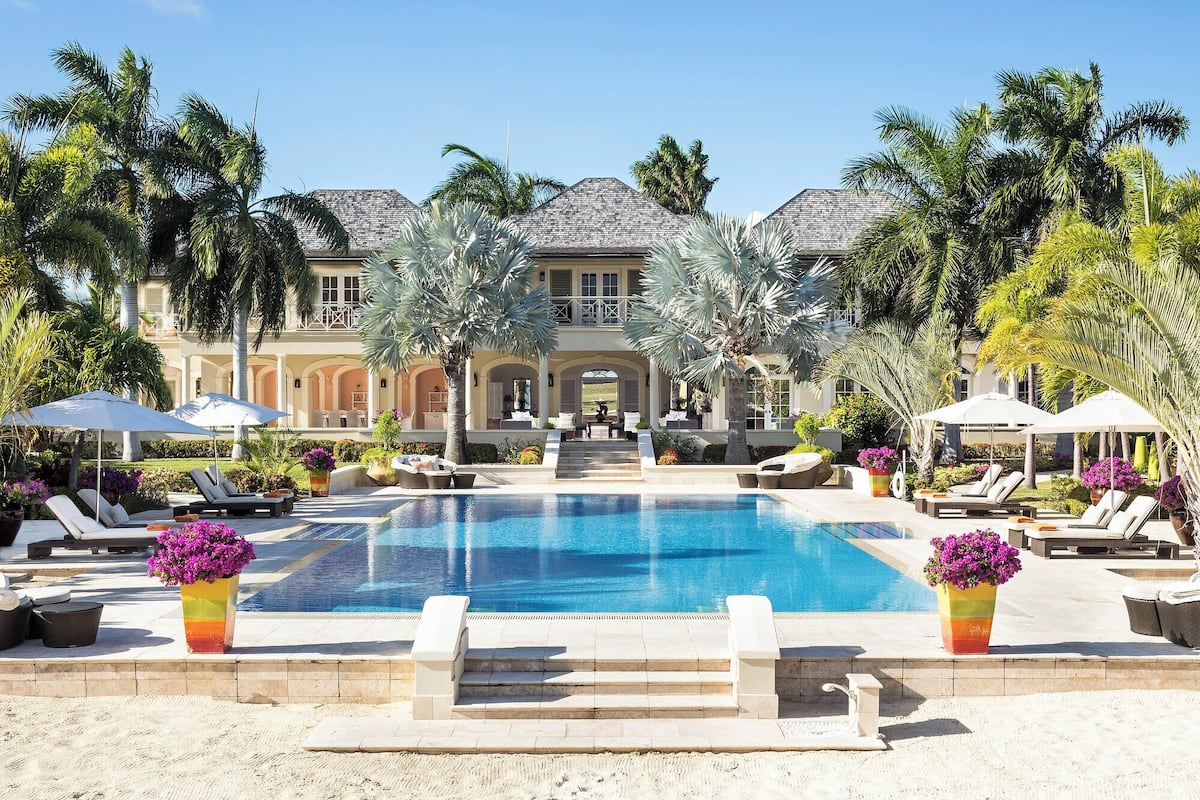 A resort with a swimming pool, lounge chairs, and palm trees.