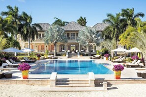 A resort with a swimming pool, lounge chairs, and palm trees. - Jumby Bay Island - Oetker Collection (Long Island)