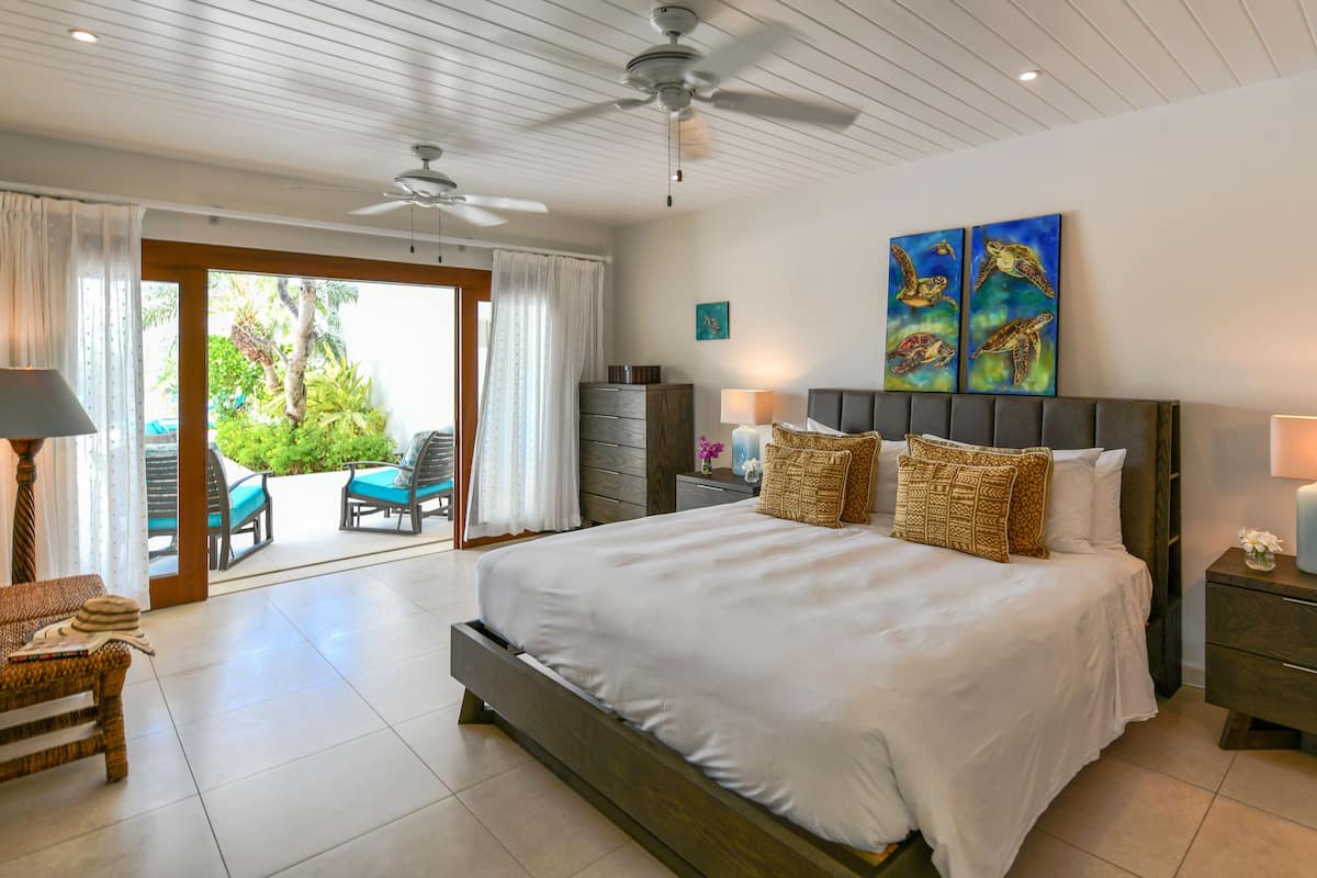 A spacious bedroom with a large bed, a ceiling fan, and a view of a balcony with outdoor furniture.