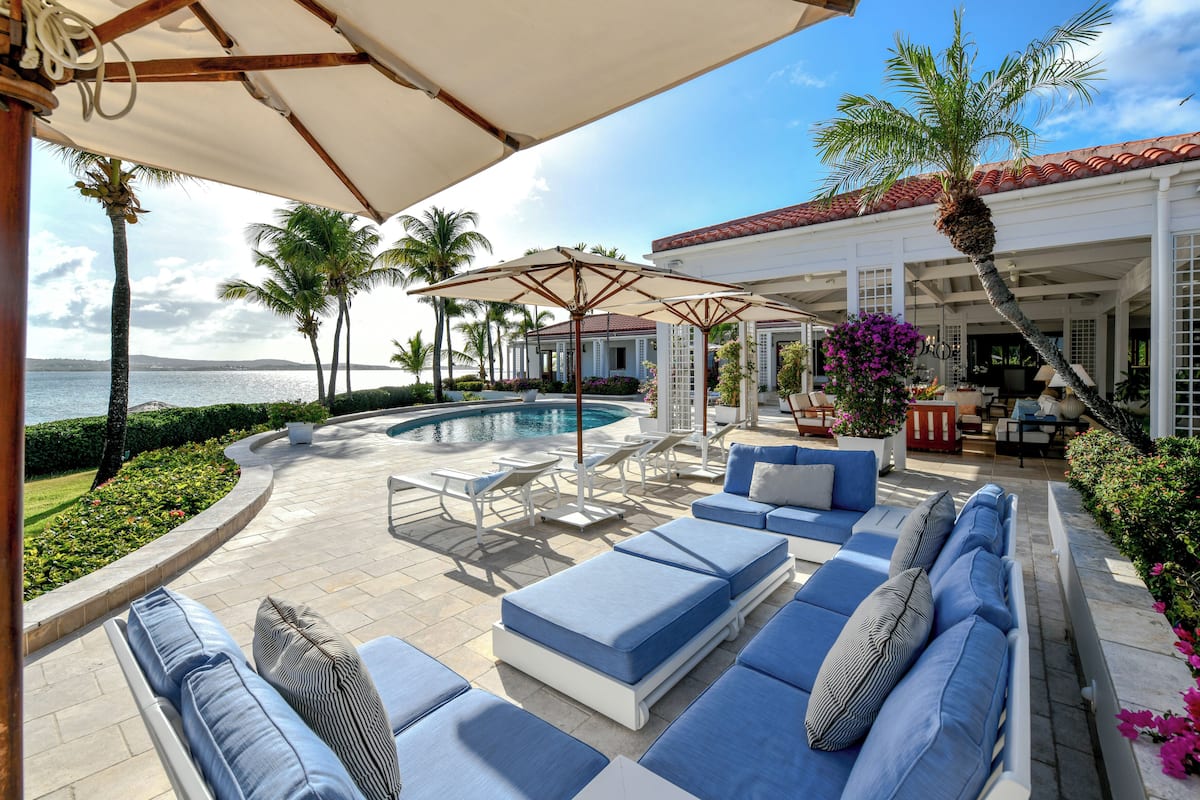 A poolside area with lounge chairs, a covered seating area, and a view of the ocean.