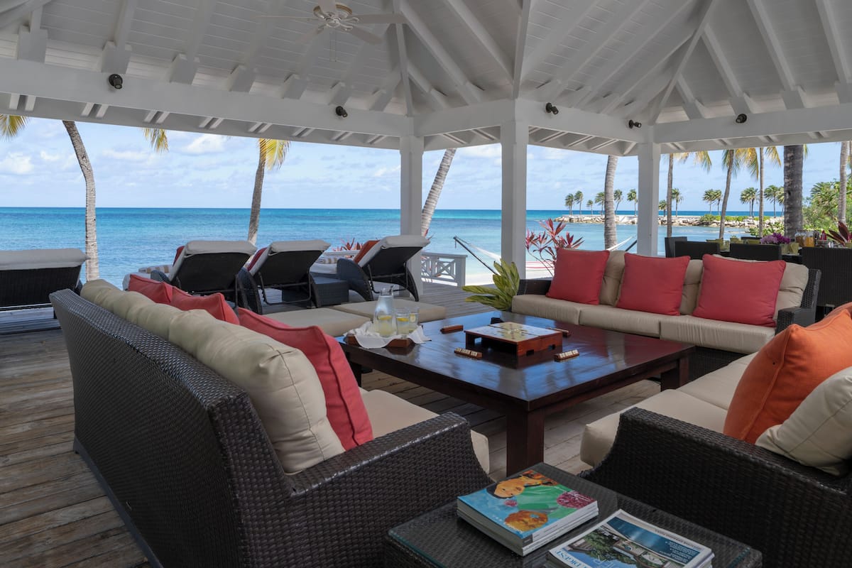 A covered outdoor seating area with wicker furniture, a wooden coffee table, and a view of the ocean.