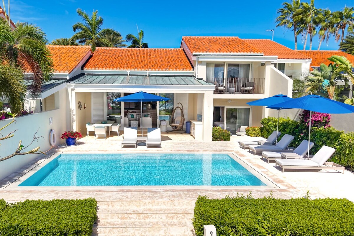 Una casa moderna con piscina, mobiliario exterior y un patio cubierto.