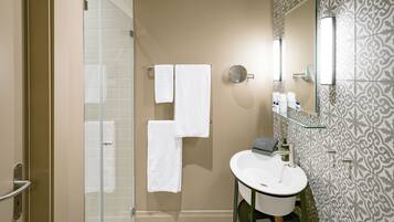 Un baño con mampara de vidrio, lavabo con espejo y azulejos estampados en las paredes.