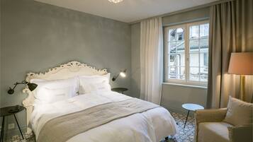 Ein Hotelzimmer mit einem großen Bett, einer Chandelier, einem fenster mit Vorhängen, einem kleinen runden Tisch und einem Stuhl.