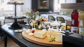 A buffet table with various cheeses, fruits, and flowers.