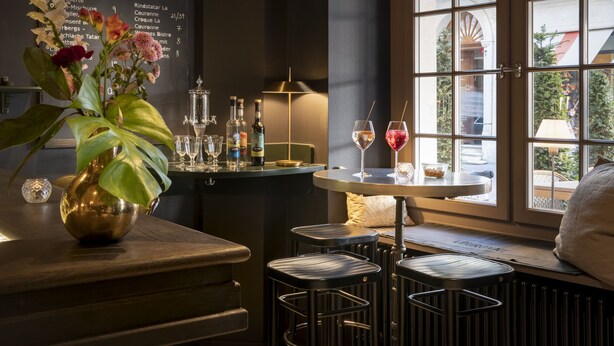 Et område med bar, menukort, barstole, et lille bord med et vinglas og et vindue med udsigt.