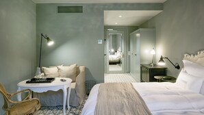 Et hotelværelse med en seng, et lille bord med stole, et skrivebord, en stol, en lampe og et spejl.