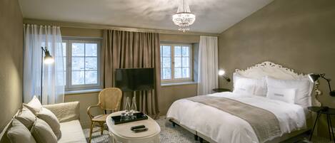 Una habitación de hotel con una cama grande, televisión, escritorio con silla y candelabro.