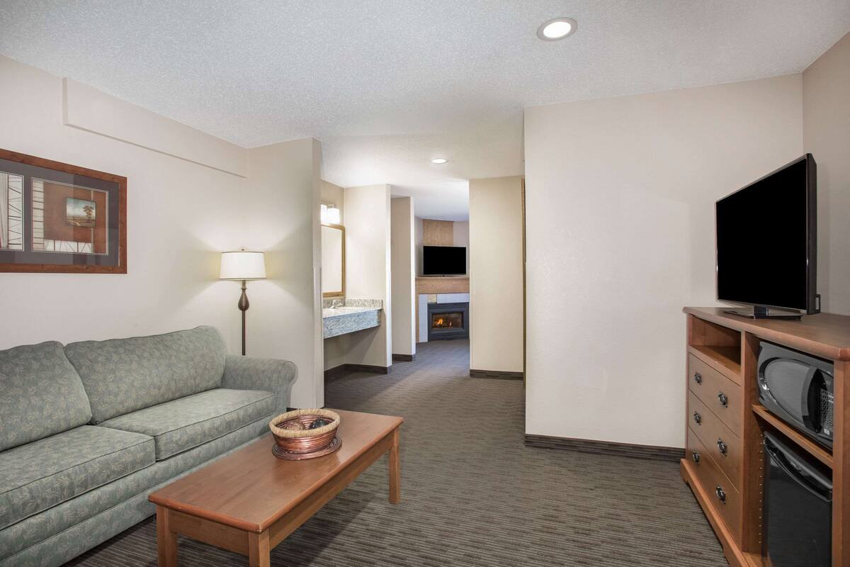 A hotel room with a sofa, a wooden coffee table, a flat-screen TV, a microwave, and a fireplace in the background.