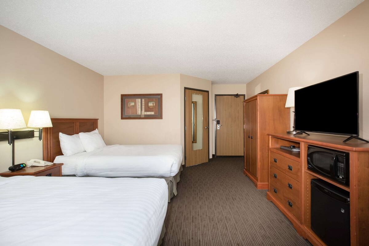 A hotel room with two beds, a television, a microwave, and a wooden dresser.