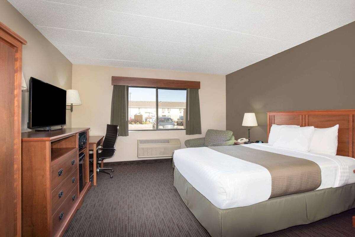 A hotel room with a large bed, a desk with a chair, a television, and a window with curtains.