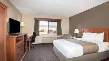 A hotel room with a large bed, a desk with a chair, a television, and a window with curtains.