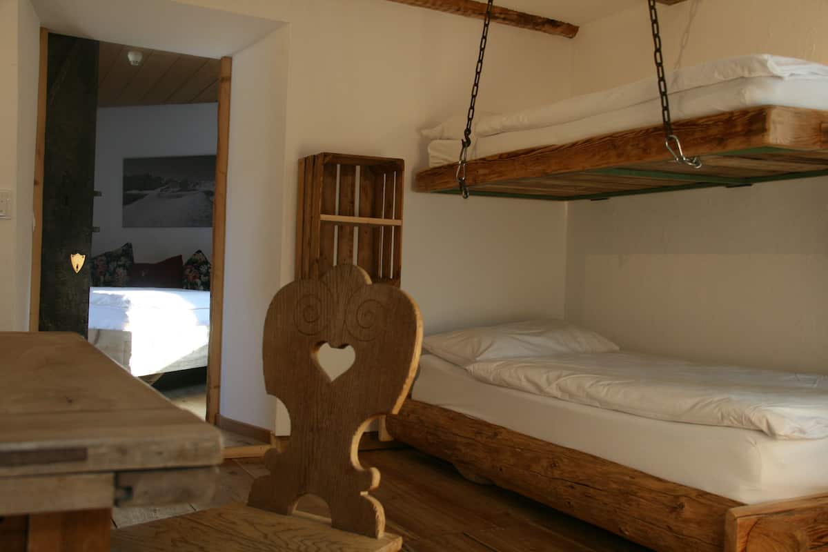 A bunk bed with a wooden headboard, a wooden table, and a bed with white bedding.