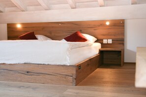 A modern bedroom with a wooden headboard, a bed with white linens and red pillows, and a small wooden nightstand.