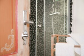 A bathroom with a shower area, a wooden chair, and a towel.